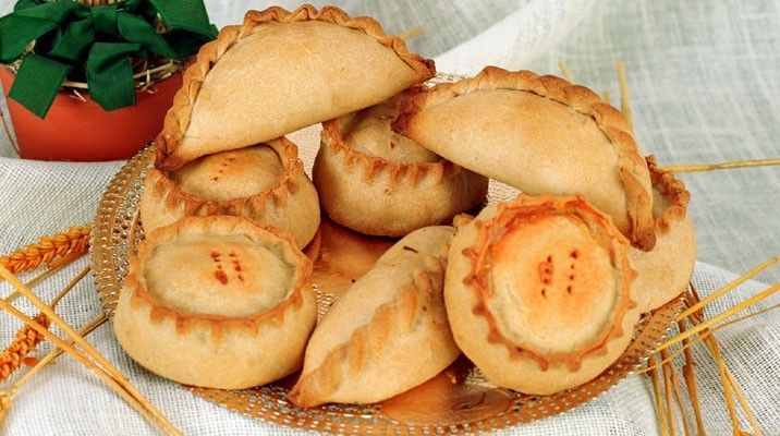 Conjunto de panades y cocarrois de masa salada colocados en una mesa con un mantel blanco de ganchillo uno encima de los otros y están debajo de un papel decorativo.dorado 
